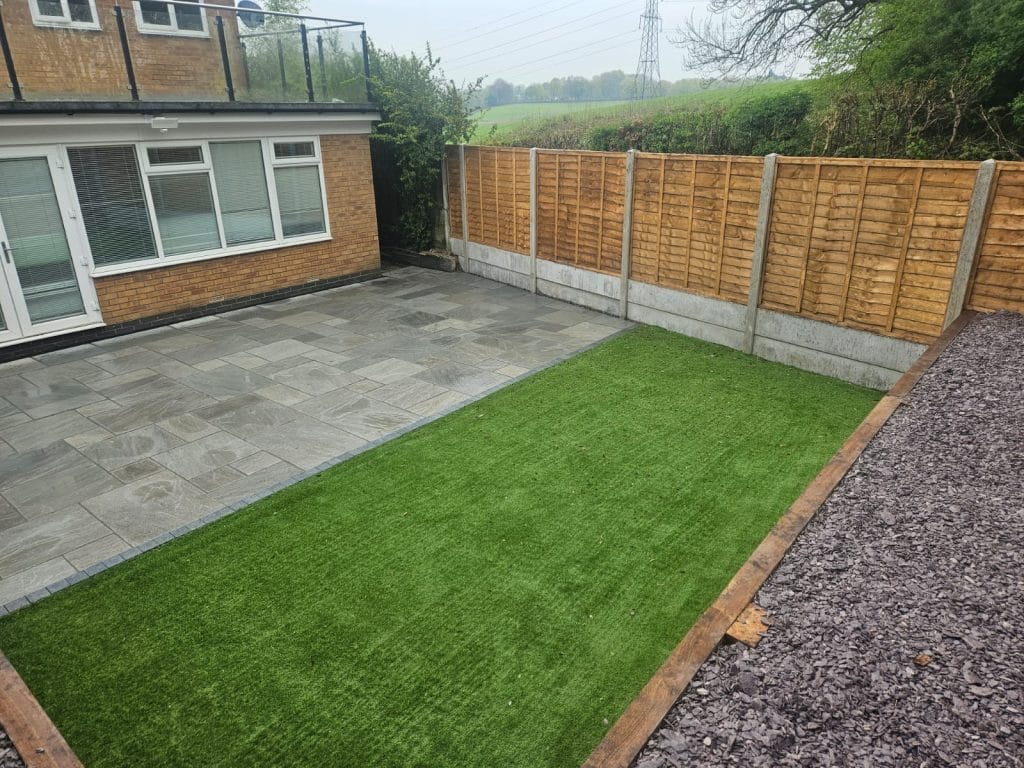 Garden with grey paving, lawn, gravel border and timber fencing